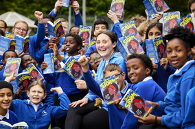 Group of children and their teacher holding up books in the air.