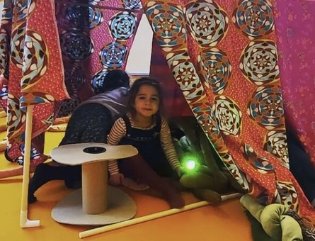 Girl in a den with soft toys around her