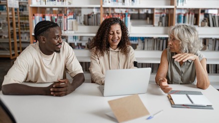Three adults sitting at a desk talking together