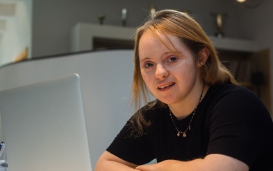 Young woman with Down's Syndrome sitting smiling by computer