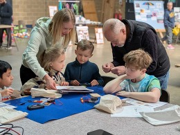 two children taking part in a team repair workshop helped by two adults