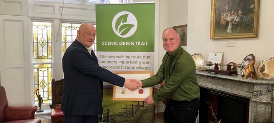 Mayor shaking hands with trail creator with logo in the backgorund