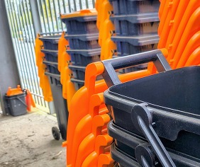A stack of black food caddy bins with orange lids at an outdoor depot