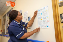 A ward nurse is pinning up a visitors charter poster on the wall