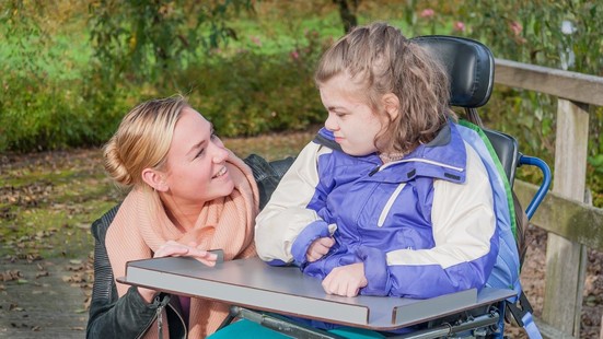 A young person in a wheelchair smiling with their parent or carer