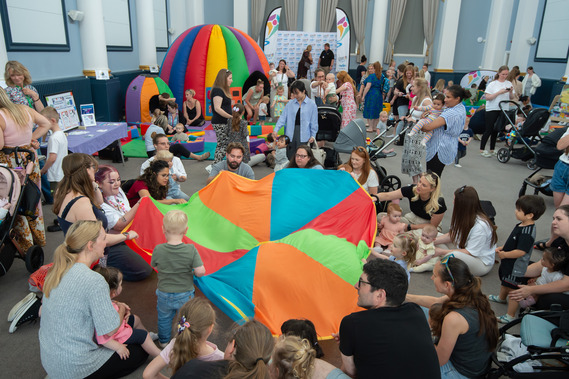 Babies, toddlers, parents, and carers taking part in a parachute game. 