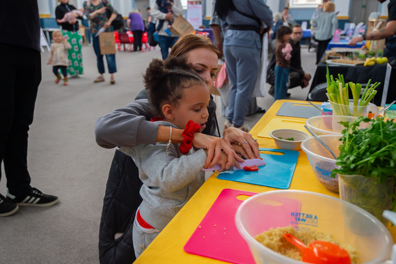 Toddler having a go at preparing vegetables with their parent/carer.