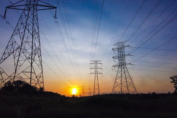 Electricity pylons and power lines silhouetted against a sunset sky.