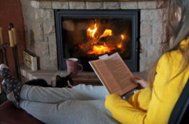 female reading book in front of a log fire