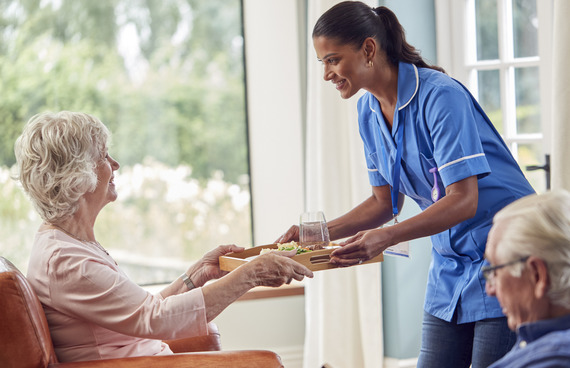Care home assistant handing over food tray at lunch time