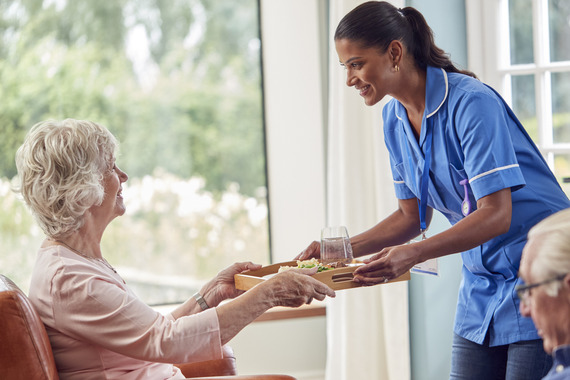 Care home assistant handing over food tray at lunch time