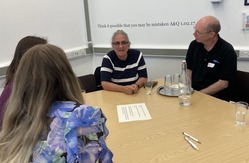 Four people seated around a table in a meeting room with papers and water glasses.