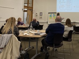 A presentation being delivered to groups of people around tables