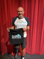 Man holding a black tote bag in front of red draped curtains