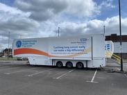 Mobile health screening unit labelled "Targeted Lung Health Check Programme" by NHS Greater Manchester, parked in an empty lot under a cloudy sky.