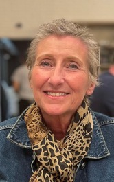 A lady with short cropped hair with a jeans jacket and scarf