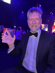 A male doctor holding up an award wearing a black and white suit