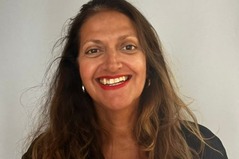 Selina with long brown hair, red lipstick, and hoop earrings against a plain light background