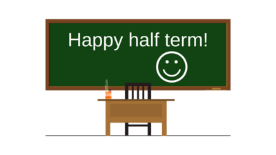 Chalkboard with the words 'happy half term' with an empty teachers desk in front. 