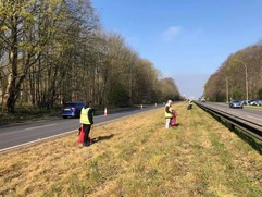 Three people in high vis collecting litter on a busy road