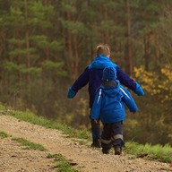 Photo of two young children walking along a gravel travel surrounded by trees