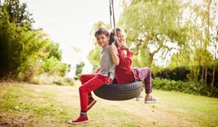 Girl and boy on a tyre swing in the garden. 