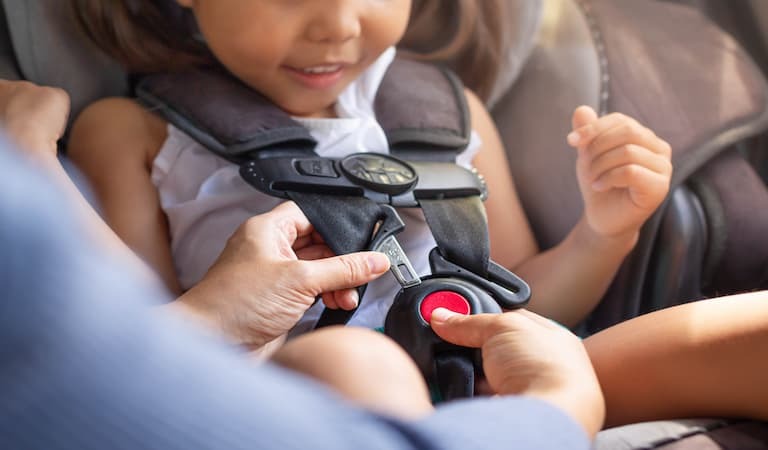 Parent buckling their child into their car seat.