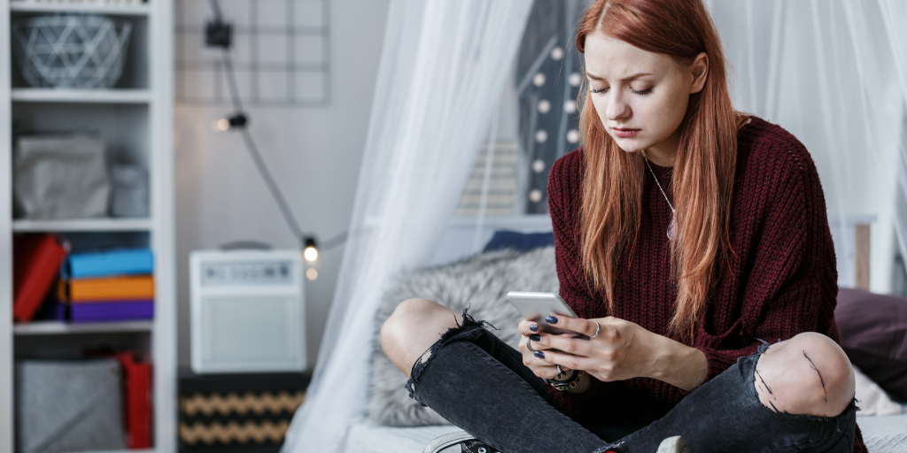 Teenage girl sat crossed legged on bed looking at phone