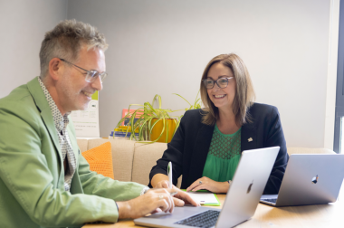 A person is sat at their laptop, working across from someone else both sat at a desk