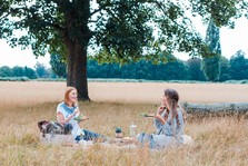 two women sitting in a field enjoying a picnic