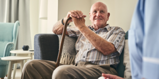Elderly man with a walking stick sitting on a sofa