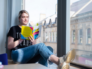 A woman sat on a windowledge reading a book
