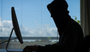 Silhouette of a man in a hoodie looking at a computer screen