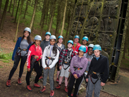 A group of children smiling in front of a climbing wall, wearing helmets and harnesses
