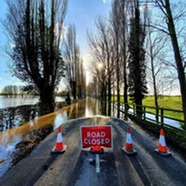 A picture of a flooded countryside road. A sign placed in the centre of the road reads "road closed". 