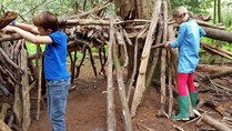 A boy and a girl build a shelter using lengths of wood in a forest