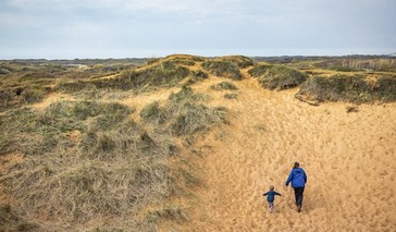 woman and child walking up a sand dune
