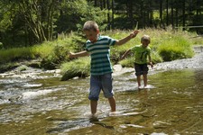 Two boys run through a shallow, slow running river
