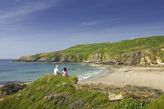 A pair sit on top of a cliff looking out on a sea view