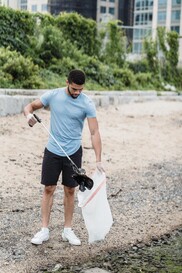 Young man clears litter from a beach with a litter picker