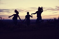 3 people jump in the air as the sun goes down