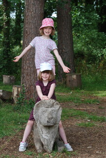 Two children stand on a wooden lion in summer clothes