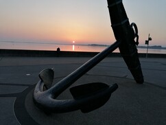 An anchor on a waterfront with the sun going down in the background