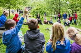 Children sit and listen in log circle in middle of forest