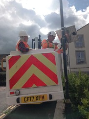Two council workers erect an air quality monitoring system to a street light pole