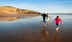 Three people run towards the sea on a beach