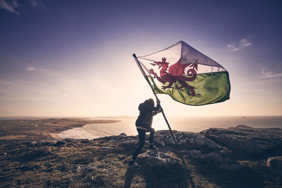 Person holding the national flag of Wales on a hill with coastline