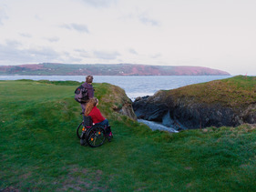 wheelchair user and walking companion on a grassy coastal path