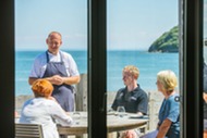 chef talking with customers at a table with seas behind him
