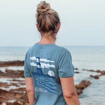 woman wearing a pale blue tshirt with a coastal design on the back